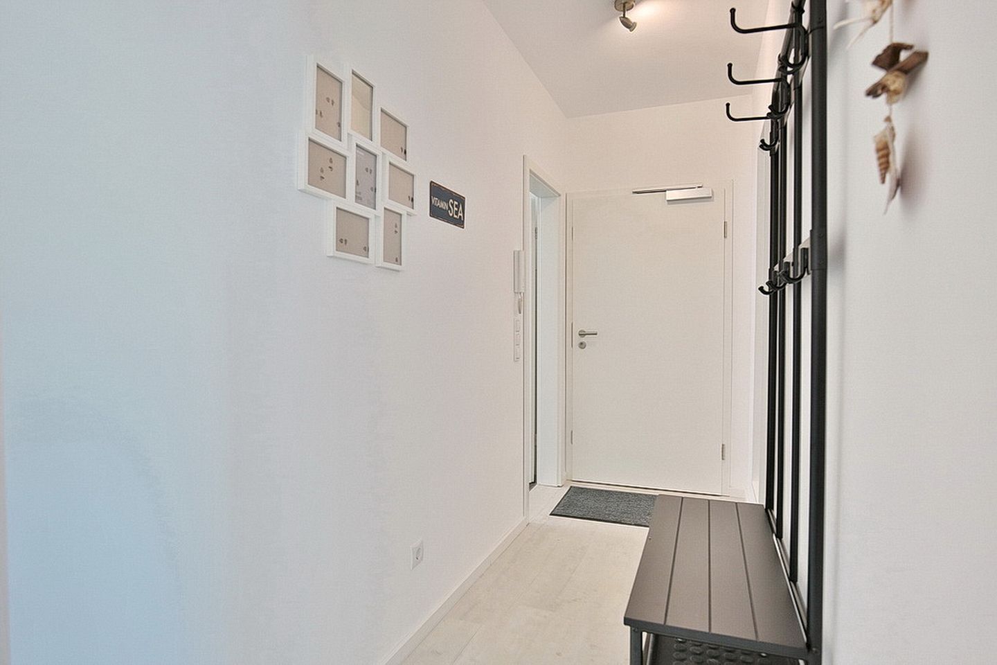 Un couloir avec un banc, un porte-manteau et une porte.