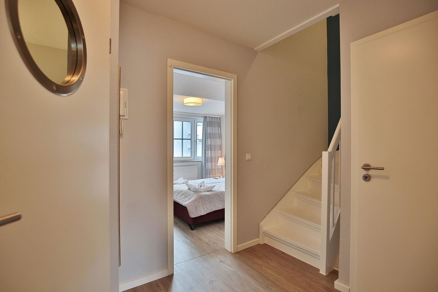 A hallway leading to a bedroom with a bed, a window, and a door.