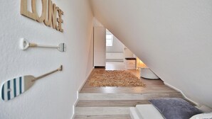 Ein Schlafzimmer im Loft-Stil mit schrägverdeckter Decke, Holzboden, einer weißen Couch und einem kleinen Teppich.