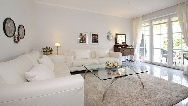 Una sala de estar moderna con un sofá blanco, una mesa de centro de cristal y un ventanal con cortinas.