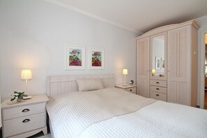 A bedroom with a bed, nightstands, a dresser, and two framed floral paintings on the wall.