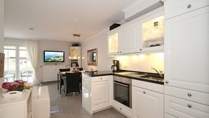 Una cocina moderna con armarios blancos, horno integrado y comedor con mesa y sillas.