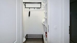 Un pasillo estrecho con un perchero metálico, un inodoro y una puerta que da a otra habitación.