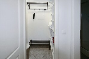 Un pasillo estrecho con un perchero metálico, un inodoro y una puerta que da a otra habitación.
