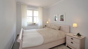 Un dormitorio con cama, mesitas de noche, ventana con cortinas y decoración en la pared.