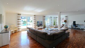 A modern living room with a sectional sofa, a flat-screen TV, a desk with a chair, and a large window with curtains.