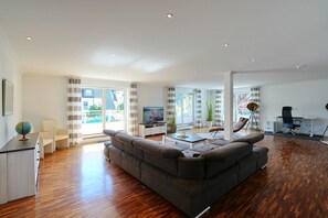 A modern living room with a sectional sofa, a flat-screen TV, a desk with a chair, and a large window with curtains. - Penthouse am Platz Beach Loft Apartment 6 - Penthouse am Platz (Timmendorfer Strand)