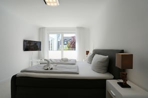 Ein Hotelzimmer mit Bett, Nachttischlampe, Fernseher und einem Fenster mit Vorhängen.
