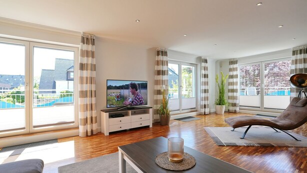 A modern living room with a TV, sofa, and a view of a swimming pool.