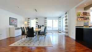 A modern dining area with a table and chairs, a kitchen counter, and a view through large windows.