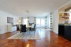 A modern dining area with a table and chairs, a kitchen counter, and a view through large windows. - Penthouse am Platz Beach Loft Apartment 6 - Penthouse am Platz (Timmendorfer Strand)