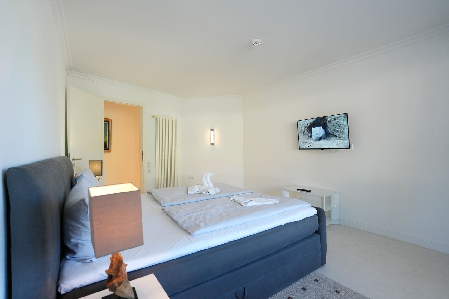 Quarto de hotel moderno com cama, mesas de cabeceira, televisão de tela plana e um quadro na parede.
