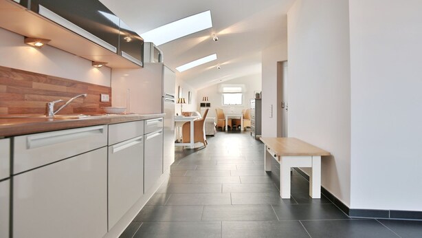 A modern kitchen with a central island, a dining area with a bench, and a view of the living room. - Penthouse am Platz Apartment 10 - Penthouse am Platz (Timmendorfer Strand)