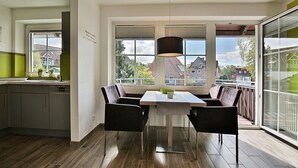 A modern kitchen with a dining area, large windows, and a view of the neighborhood.