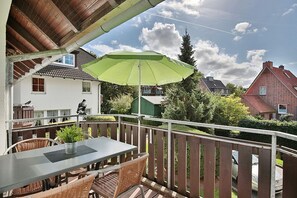Un balcón con mesa y sillas, un paraguas verde y vistas a casas vecinas.