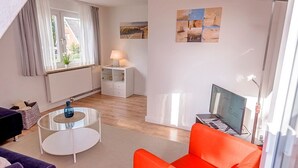 Un salon moderne avec un canapé, une table basse, un téléviseur et des œuvres d’art accrochées au mur.