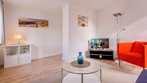 Un salon moderne avec une table basse en verre, un canapé rouge, un téléviseur et un meuble blanc agrémenté d’objets décoratifs.
