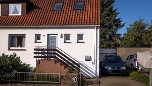 Une maison à deux étages, avec un toit recouvert de tuiles rouges, un escalier menant à l’étage supérieur et un mur de pierre à l’avant.