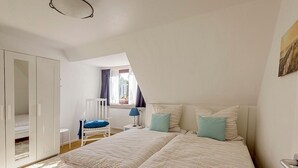 Une chambre à coucher avec un lit, une chaise, une armoire et une fenêtre avec des rideaux.