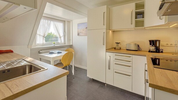 Une cuisine compacte équipée d’un évier, d’une cuisinière et d’un petit coin repas avec une chaise et une table.