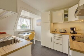 Una cocina compacta con fregadero, estufa y un pequeño comedor con una silla y mesa.
