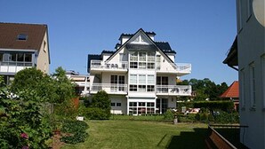 Un immeuble à plusieurs étages doté de balcons, d’une pelouse bien entretenue et entouré de verdure.