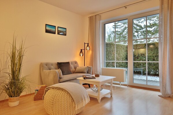 A cozy living room with a sofa, a small table, and a large window with a view of trees.