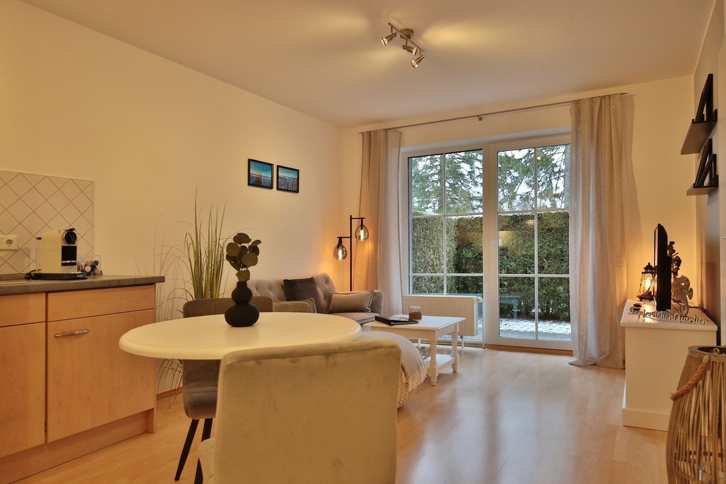 A modern living room with a dining area, large windows, and a view of greenery.