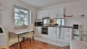A modern kitchen with white cabinets, a wooden dining table, and a window with blinds.