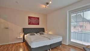 A modern bedroom with a large bed, a red abstract painting, and a large window with blinds.