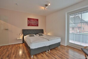 A modern bedroom with a large bed, a red abstract painting, and a large window with blinds.