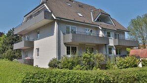 A multi-story residential building with a grey brick facade, multiple balconies, and a sloped roof.