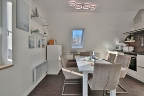 Una cocina moderna con comedor, que presenta una mesa blanca, sillas grises y un ventanal con vista a árboles.