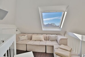 Camera da loft moderna con un'ampia finestra, un divano angolare beige e una scala bianca.