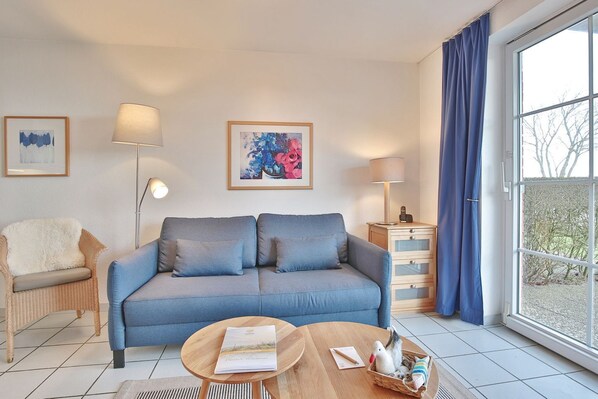A modern living room with a blue sofa, two side tables, a floor lamp, and a large window with curtains.