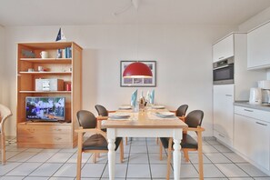 Un salon moderne comprenant une table à manger pour quatre personnes, un téléviseur, une bibliothèque et un coin cuisine équipé d’un four à micro-ondes et d’un four traditionnel.