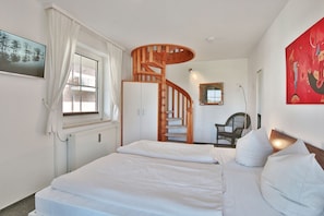 Ein Schlafzimmer mit einem Bett, einer Wendeltreppe aus Holz, einem Sessel und einem Gemälde an der Wand.