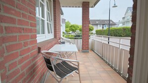 Een balkon met een tafel en stoelen, een bakstenen muur en een witte reling.