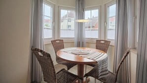 Een zithoek met eethoek, met een ronde tafel, vier rieten stoelen en een hanglamp.