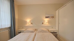 Een tweepersoonskamer met twee bedden, nachtkastjes, wandlampen en een schilderij aan de muur.