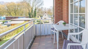 A balcony with a white table and chairs, a potted plant, and a view of a building and trees.