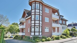 A multi-story residential building with a corner design, featuring balconies and a brick facade.