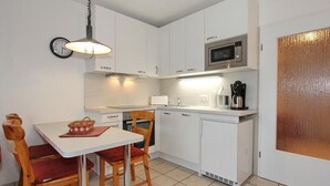 A compact kitchen with white cabinets, a microwave, a coffee maker, and a dining area with two wooden chairs and a table.