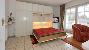 A bedroom with a bed, a TV, a chair, and a wardrobe.