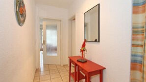 A hallway with a red table and a decorative parrot sculpture, a frosted glass door, and a mirror on the wall.
