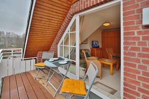 A cozy attic bedroom with a wooden sloped ceiling, a small dining table with chairs, a sofa, and a television.