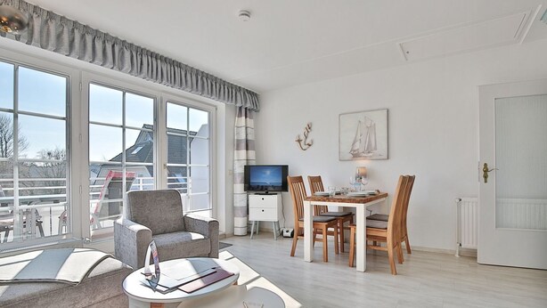 A modern living room with a sofa, a dining table with chairs, a TV, and a large window with curtains.