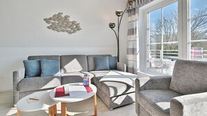 A modern living room with a grey sectional sofa, a white coffee table, and a large window with a view of trees.
