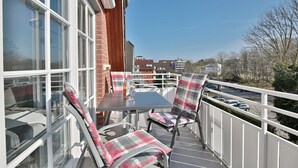 A balcony with a table and chairs, a brick wall, and a view of the street.
