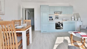 A compact kitchen with light blue cabinets, a built-in oven, and a dining area with wooden chairs and a table.